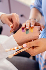 Obraz na płótnie Canvas Closeup hands of professional female visagist applying colorful swatches of trendy eyeshadow
