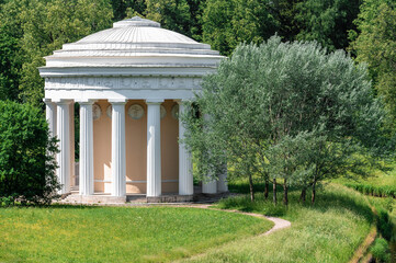 a classical-style temple in a beautiful summer park Green field with white and yellow dandelions outdoors in nature in summer. Bright green summer field at daytime