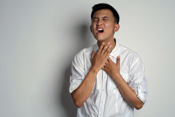 Portrait of young asian man having bad sorethroat and touching his neck using his hands, against white background. Man having sorethroat. Symptoms of contracting virus concept. CORONA VIRUS COVID-19