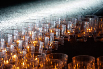 burning candles in transparent plastic cups, memory action, dark background, evening time, live fire, candle flame