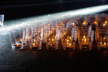 burning candles in transparent plastic cups, memory action, dark background, evening time, live fire, candle flame
