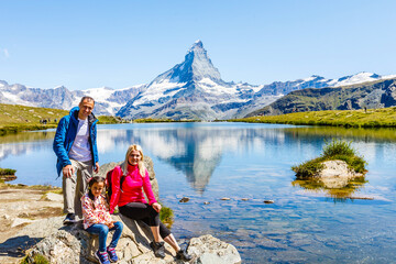 Happy family with little child doing trekking on switzerland mountain in summer time. Young people...
