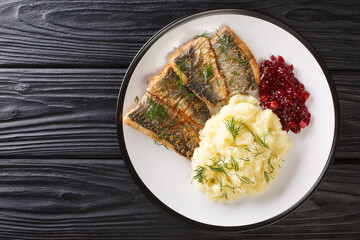 Fried herring fillets with mashed potatoes and lingonberry sauce close-up in a plate on the table....