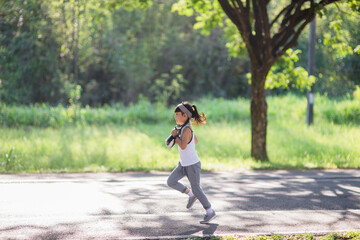 Fototapeta na wymiar happy child girl running in the park in summer in nature. warm sunlight flare. asian little is running in a park. outdoor sports and fitness, exercise and competition learning for kid development.