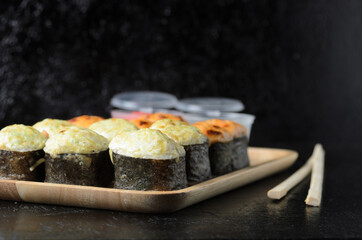 A set of seafood rice rolls wrapped in thin dried sea grass leaves on a wooden platter with ginger and wasabi