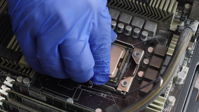 Electronics repair technician with a blue glove carefully installs a computer processor into a socket on the motherboard of a desktop computer. View from the inside of a personal computer system