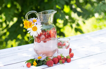Homemade strawberry mojito lemonade in a glass jug on a white wooden rustic table. Strawberries, mint sprigs and flowers. Summer ice cold drink.	