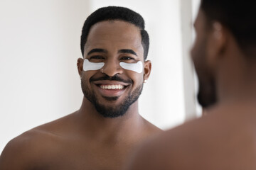 Happy attractive African American guy with applied collagen gel patches on under eye skin smiling...