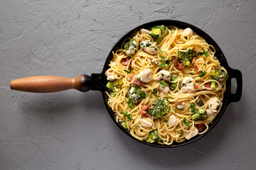 Homemade Chicken Bacon Broccoli Alfredo in a cast-iron pan on a gray surface, top view. Flat lay, overhead, from above.