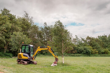 Small yellow color excavator with bucket attached to the arm in a park. Heavy machinery equipment....