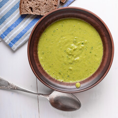 Bowl of creamy pea and herb soup on the table with pieces of bread