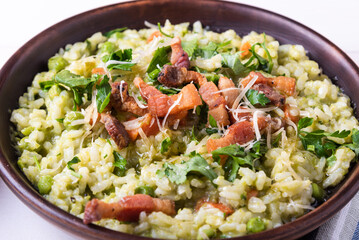 Homemade risotto with peas and fried crispy bacon, pancetta and grated cheese on a plate, close-up