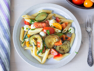 Warm summer Italian salad with pasta, fried zucchini, tomatoes and mozzarella cheese on a plate