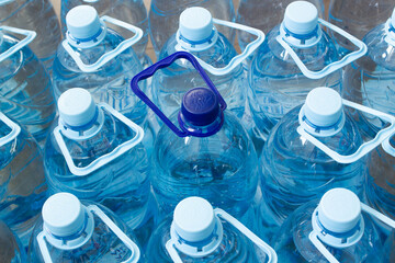 Many blue plastic bottles with blue caps and one with dark blue cap with clear mineral water in a...