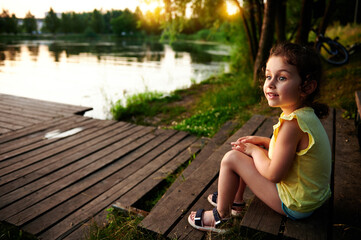 A charming girl resting on the pier and looking into the distance against the backdrop of the river bank. Camping, summer themes.