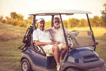 Two older friends are riding in a golf cart.