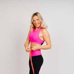 Fitness woman with tape measure showing her waist on studio background