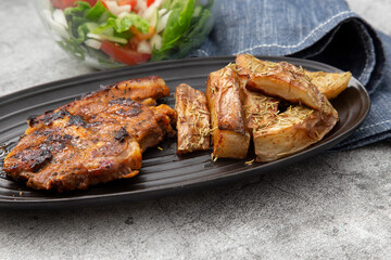 Minted lamb chop on a black dish with rosemary covered potato wedges and salad