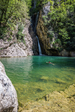 A scenic waterfall falling among a rocky gorge with a swimming male figure. Agur river in Khosta microdistrict, Russia. Travelling, hiking, mountain activities, outdoors and scenic destinations.