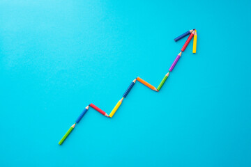 Flat lay of color pencils graph growth up form on blue background with copy space. Business growth, creative idea, kids art education and development concept.