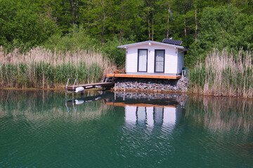 Kleines Ferienhaus am Ufer des Hainer Sees, umgeben von Schilf, mit Steg und Spiegelung, Hainer See, Sachsen, Deutschland