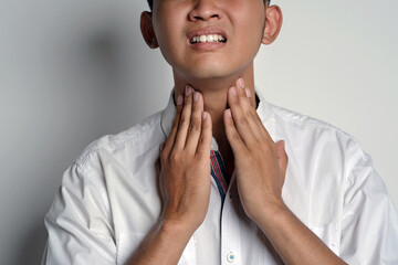 Close up portrait of young asian man having sore throat and touching his neck using his hands,...