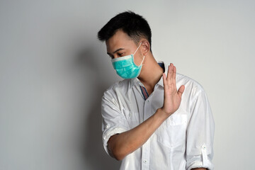 Portrait of young asian man wearing health mask standing with face turn to the right and showing refusal gesture againsat white background. Symptoms of contracting corona virus concept. COVID-19
