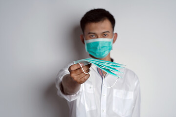 Portrait of young asian man wearing mask and offering/giving mask while looking at to the camera aginst white background. Symptoms of contracting corona virus concept. Novel Coronavirus (COVID-19)