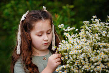 Selective focus. Portrait of a girl in a green dress with a bouquet of daisies in nature. The girl holds a large bouquet of camomiles in front of her and examines the flowers.