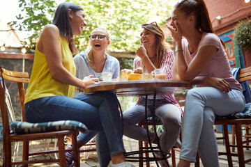 group of cheerful, relaxed, female friends, sitting in outdoor cafe, laughing