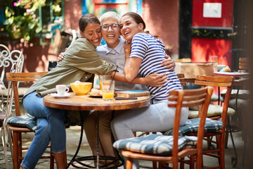 Fototapeta na wymiar mother and daughters relationship concept. three caucasian women, two young and one elderly, hugging each other, sitting in outdoor cafe, smiling.