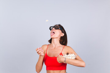 Beautiful woman on gray background in 3d cinema glasses with popcorn, cheerful happy positive emotions throws popcorn