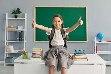 Happily. Back to school. Funny schoolgirl raised her thumb up in class. Education college school courses for children.