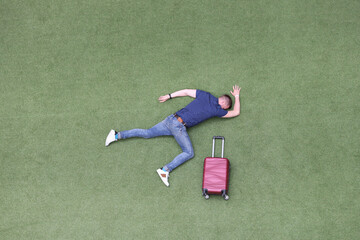 Motionless man lies on green lawn with suitcase