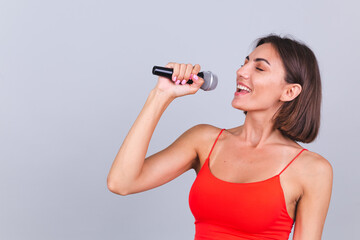Beautiful woman on gray background with microphone singing emotional favorite song happy positive...
