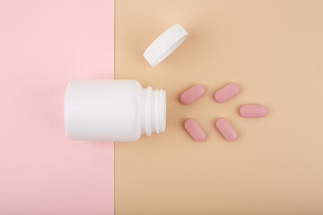 Creative flat lay with white opened medication bottle with oval pink spilled pills against pastel...