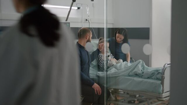 Sick daughter wearing oxygen nasal tube lying in bed after illness surgery waiting for medical examination with parents in hospital ward. Hospitalized child recovering after flu isickness nfection