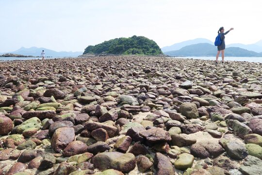 A person taking photos and  walking along the tombolo rocky path to the other end of Sharp Island