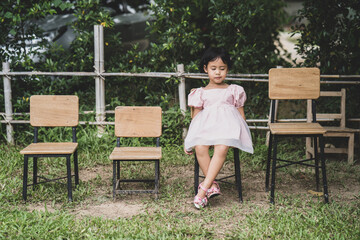 Adorable little Asian girl sitting on wooden chair at field