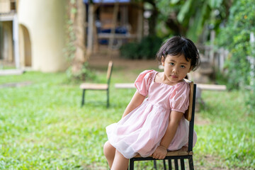 Adorable little Asian girl sitting on wooden chair at field