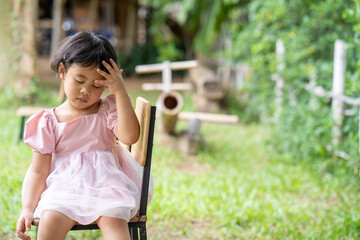 Pretty little girl with sad expression face sitting on wooden chair outdoor.