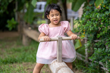 Adorable little girl playing bamboo wooden seesaw at garden.