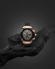 Beautiful gold men's watch with a black strap on a wooden stand, on a gray background. Beautiful gold watch. A luxury brand watch