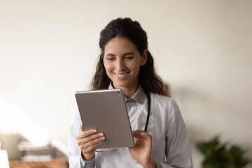 Smiling female nurse use modern table gadget in modern private hospital. Happy Caucasian woman...