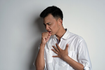 Portrait of young asian man having cough and touching his chest using his hand against white background. Symptoms of contracting the virus concept. Novel Coronavirus (COVID-19)
