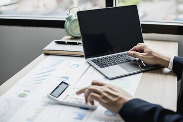 Fototapeta premium Man using laptop and pressing calculator, business man sitting in private office at his company, he runs a startup company, he's a young man starting a business. Management concept of startup company.