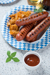 Grilled bratwurst sausages with sauerkraut on a blue and white disposable carton plate, vertical shot on a beige granite background