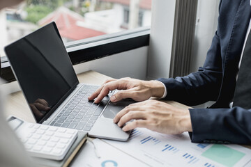 Fototapeta premium Man in suit sitting at work and using a laptop, he is a young businessman who founded a startup, he is typing text messages with his partner through an online messenger on his laptop.