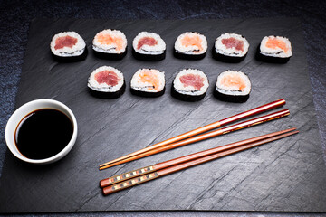 Delicious Japanese sushi next to a bowl of soy juice and wooden chopsticks on a black board. Oriental food concept