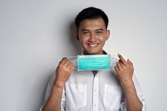 Portrait of young asian man holding a mask while smiling to the camera against white background. Prevention of the spread of corona virus photography concept. Novel Coronavirus (COVID-19)